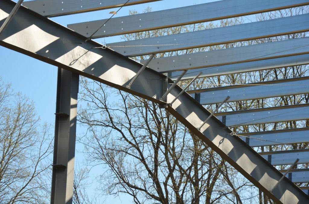 Steel beams form a structure against a clear blue sky, with bare trees in the background.