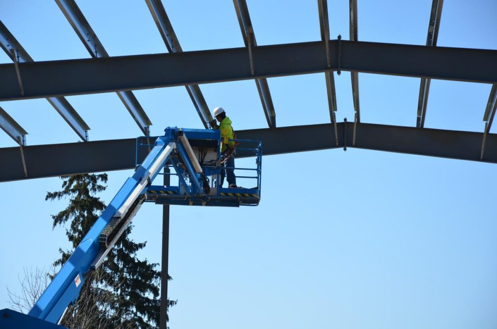 Large open metal barn with two garage doors, set on a grassy area under a partly cloudy sky.