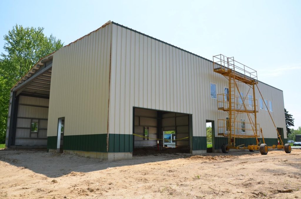 Large metal building under construction with an open doorway and scaffolding on the side.