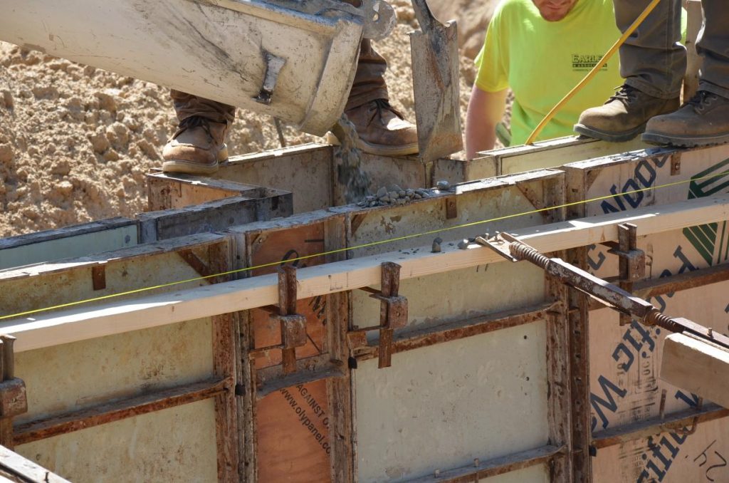 Construction workers pour concrete into a wooden formwork for a foundation.