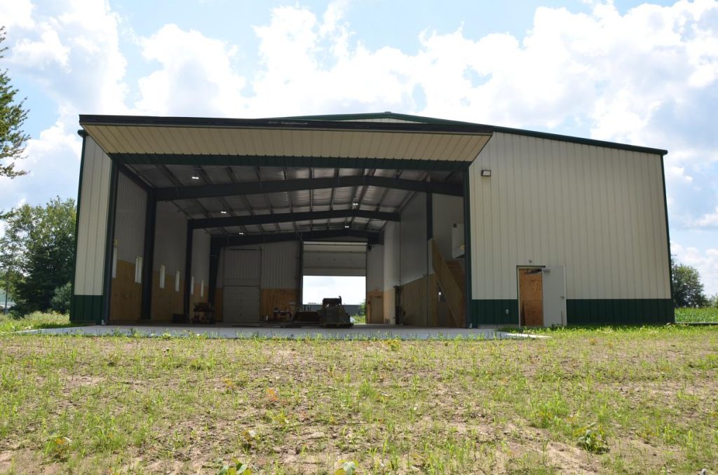 Large open metal barn with two garage doors, set on a grassy area under a partly cloudy sky.