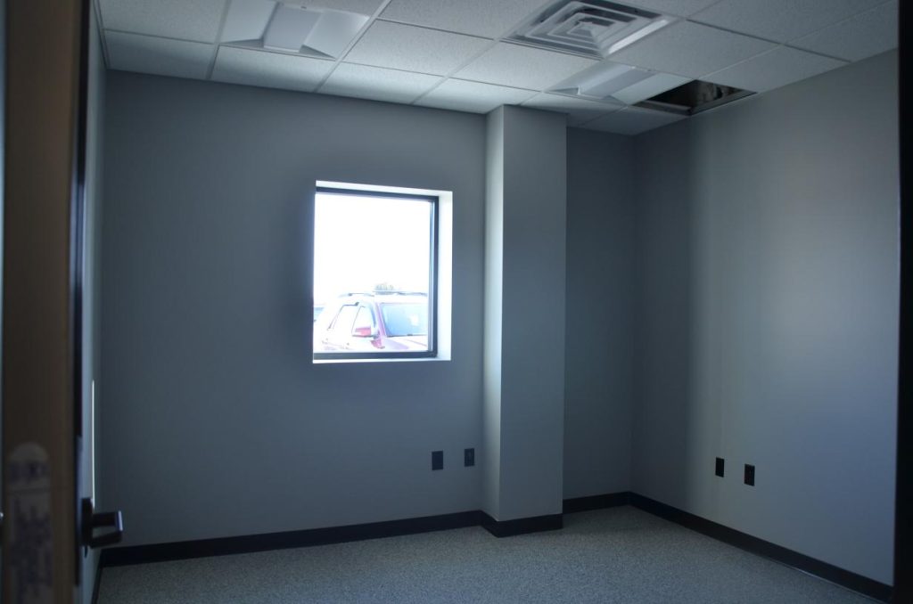 Empty room with gray walls, a single window showing a parked car outside, and a ceiling with an exposed panel.