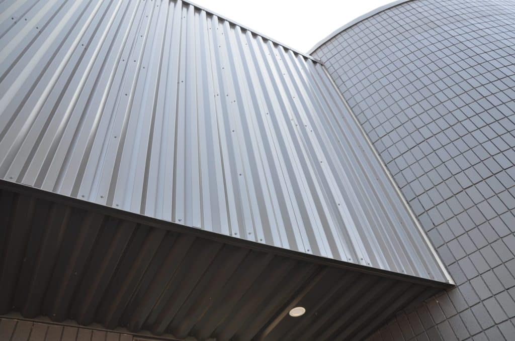 A close-up upward view of a building exterior featuring vertical metal siding next to a curved wall with rectangular tiles.