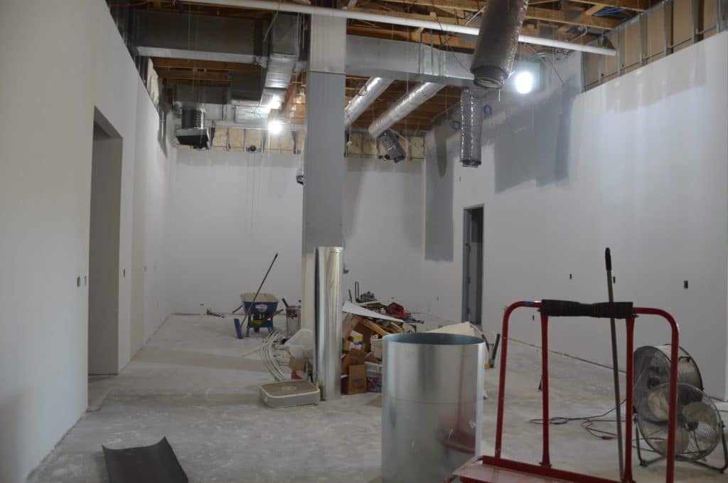 A room under construction with unfinished walls, exposed ceiling ducts, scattered tools, construction materials, and equipment.