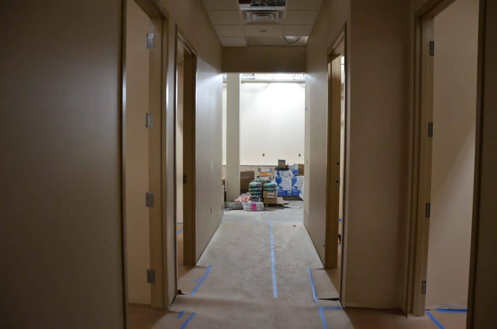 A hallway with beige walls and four open doors, leading to a room containing stacked construction materials and supplies.
