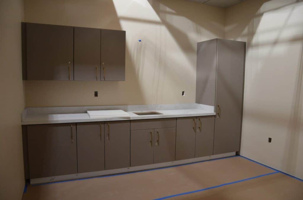 A modern kitchen under construction with taupe cabinets, a white countertop, and unfinished details, including uninstalled hardware and no appliances.