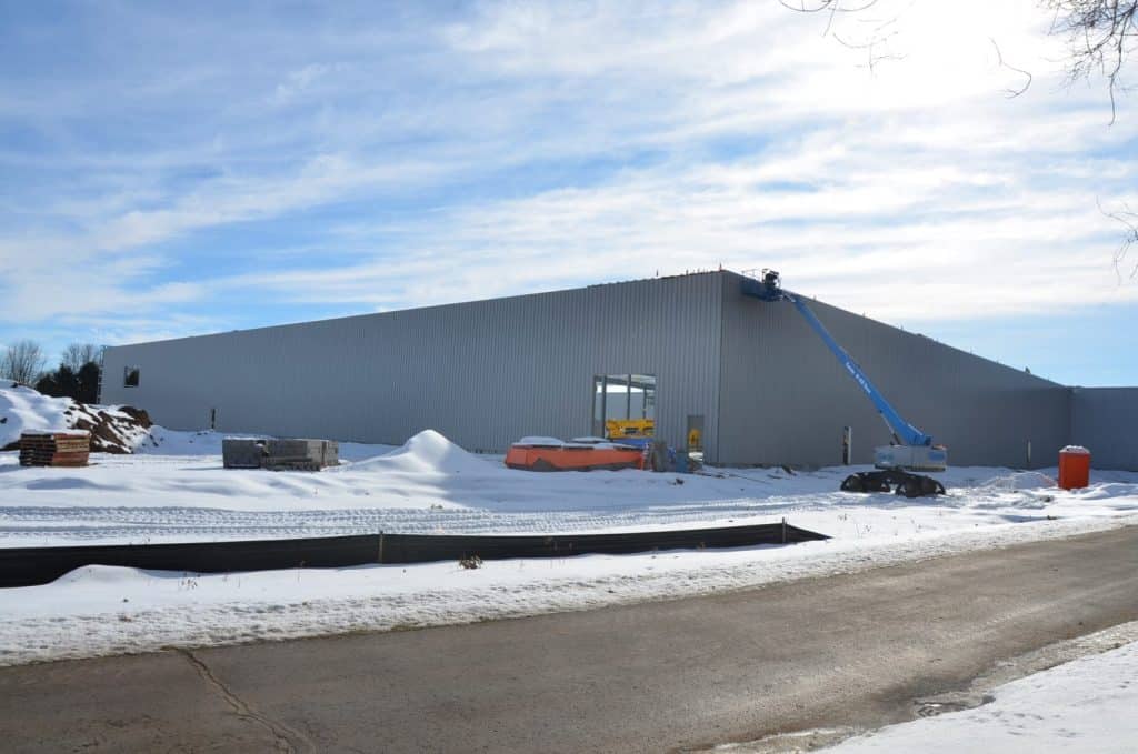 A large industrial building under construction in a snowy area, with construction equipment and materials visible outside.