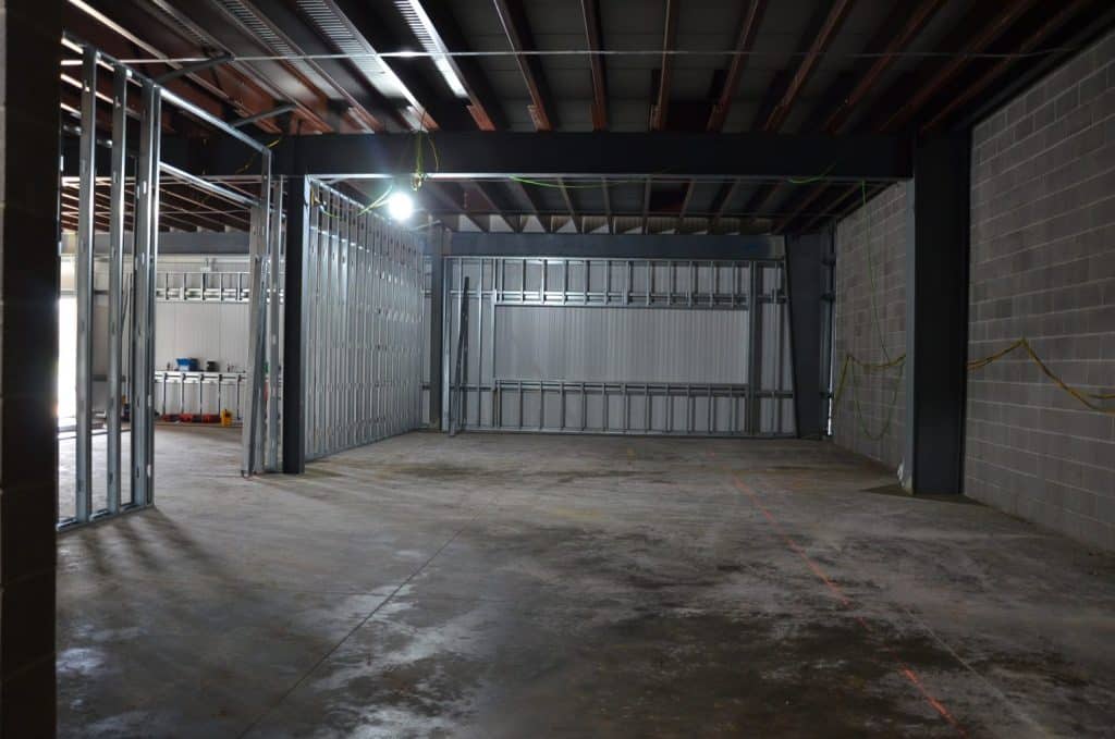 Unfinished interior of a building with exposed steel framing, concrete floor, cinder block walls, and visible overhead beams.