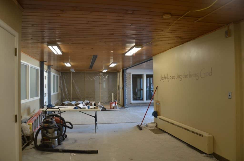 A room under renovation with construction materials and tools; a plastic sheet separates work areas. Text on the wall reads, "Joyfully pursuing the living God.