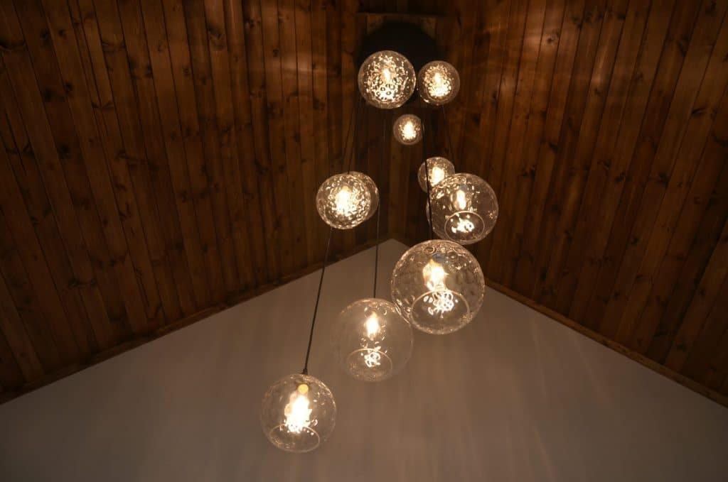 A cluster of glass pendant lights hangs from a wooden vaulted ceiling, with warm bulbs illuminating the space below.