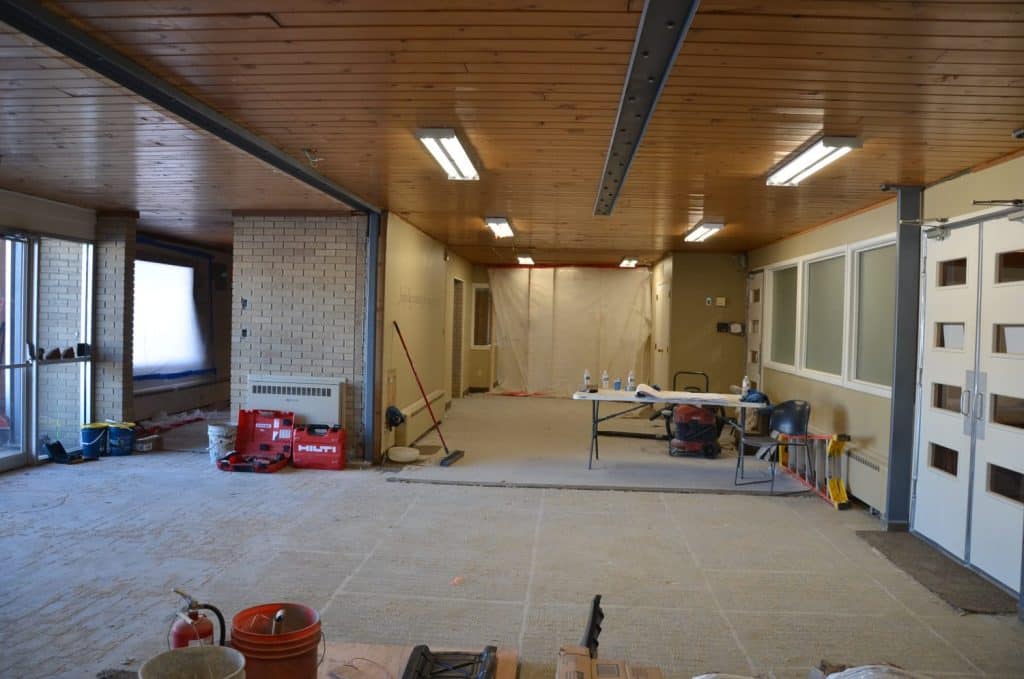 Unfinished room under renovation with exposed floor, construction tools, a table with supplies, and plastic sheeting covering the far wall.